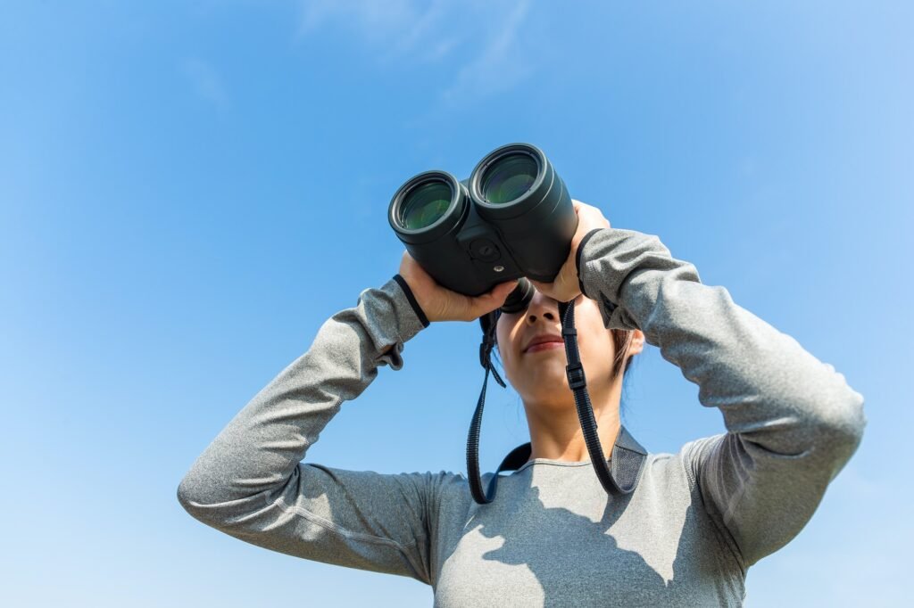 Woman watching though binoculars against the blue sky